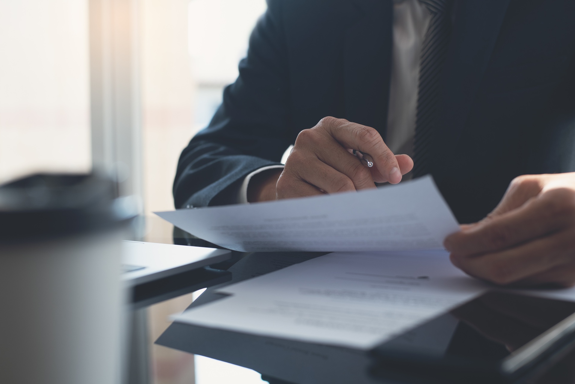 A person wearing a suit sits at a desk reviewing documents.