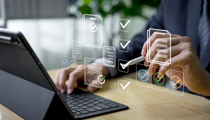A person sitting behind a tablet holds a pen up to floating document graphics.