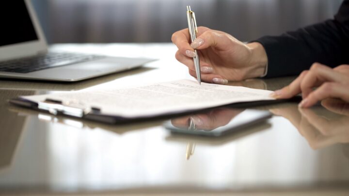 A zoomed in picture of someone going over contracts while holding a pen