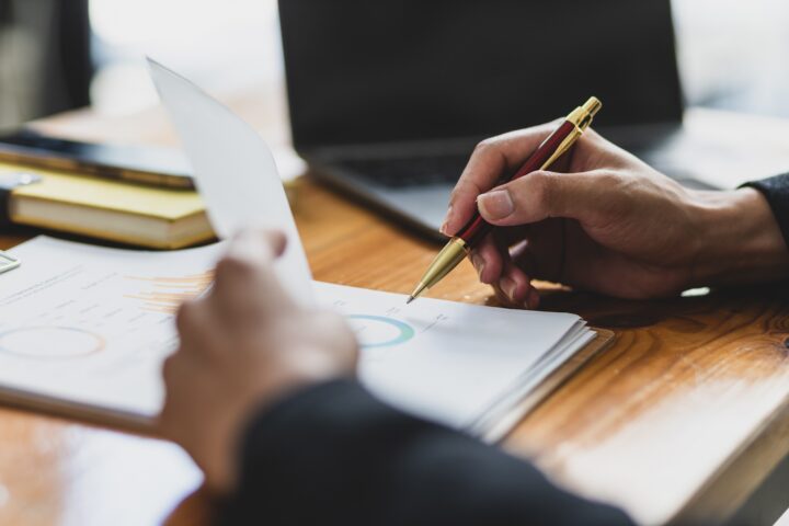 A person sits at a desk holding the front sheet in a packet of paperwork while holding a pen.